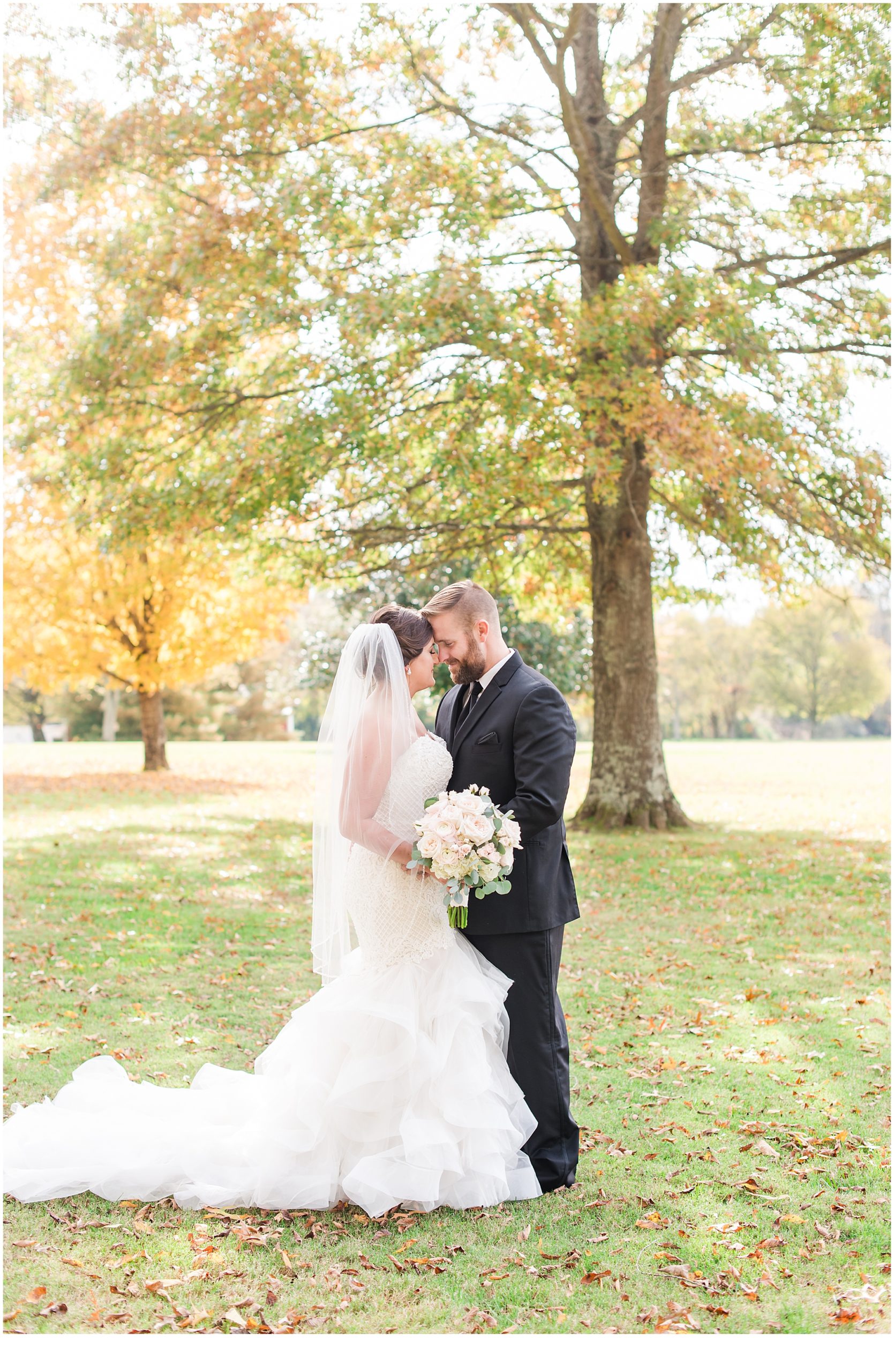 Bride & groom standing in front of fall trees.