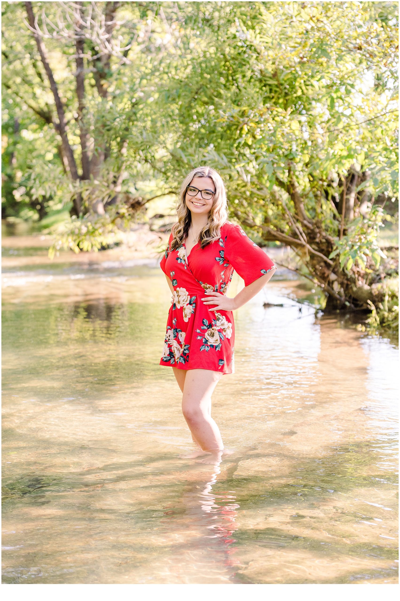 Noelle wearing a red outfit in the creek with trees in the background for her Hendersonville Creek senior photos.