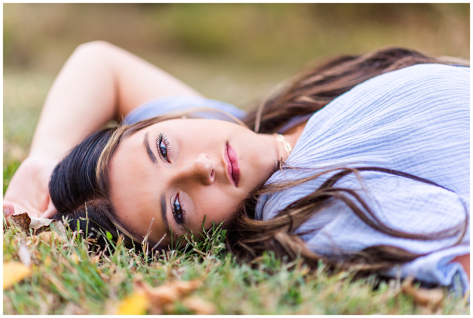 High school senior girl wearing a lavender-colored dress, laying in the grass.