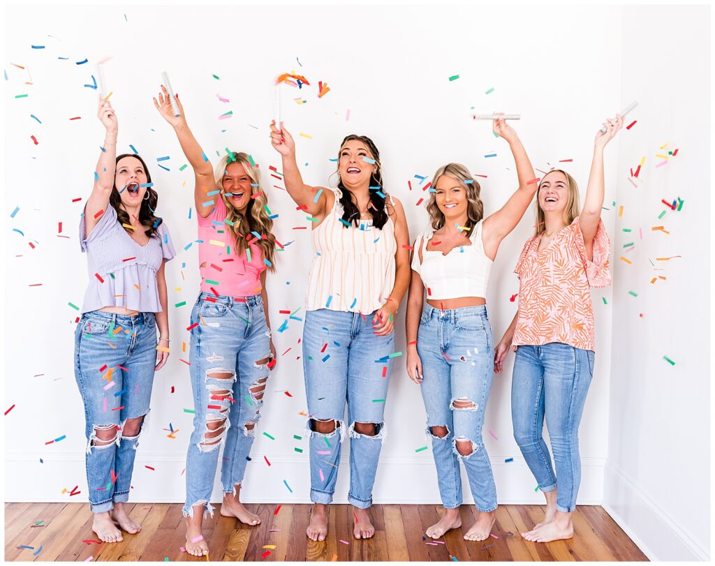 Five high school senior spokesmodels laugh as they shake confetti wands for photos. 