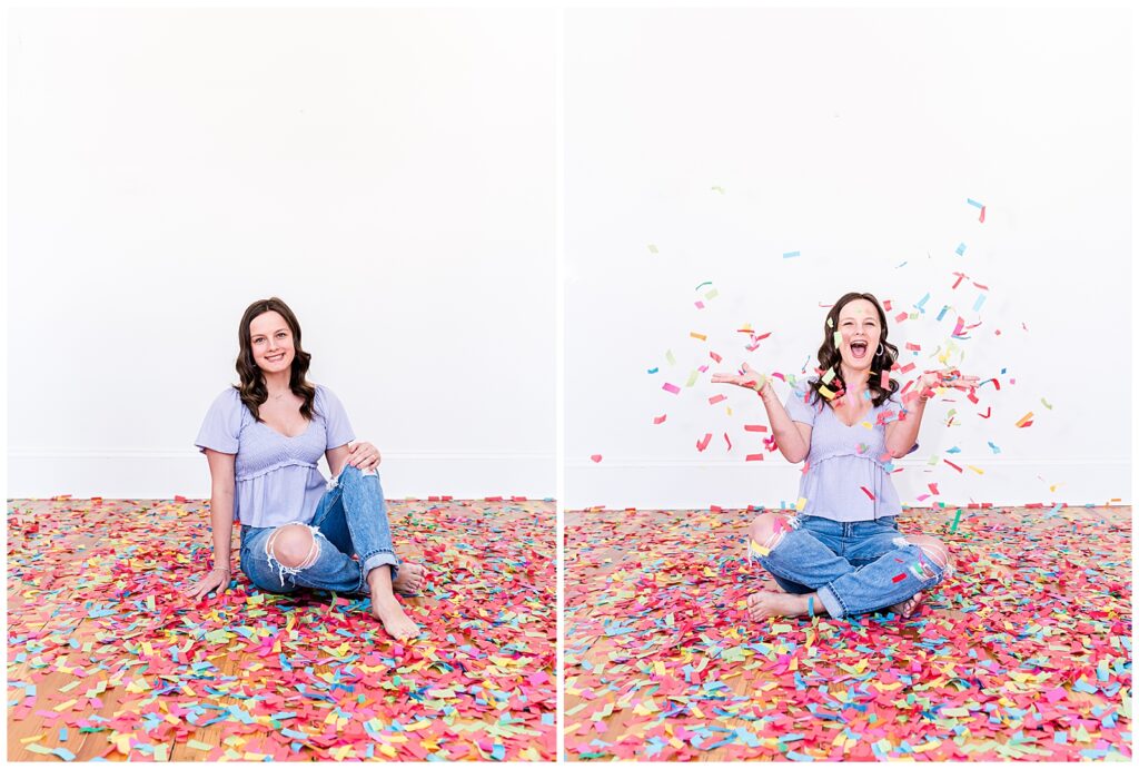 A high school senior spokesmodel wearing jeans and a purple top sits on the floor laughing as she throws confetti up in the air for pictures.