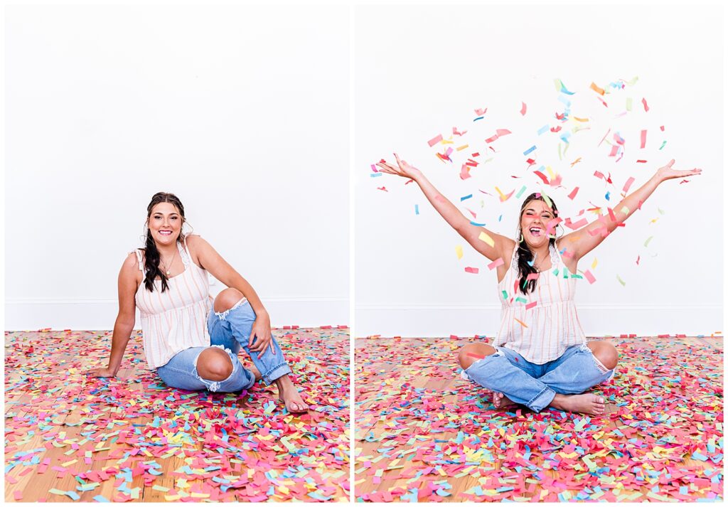 A high school senior spokesmodel wearing jeans and a cream top sits on the floor laughing as she throws confetti up in the air for photos. 