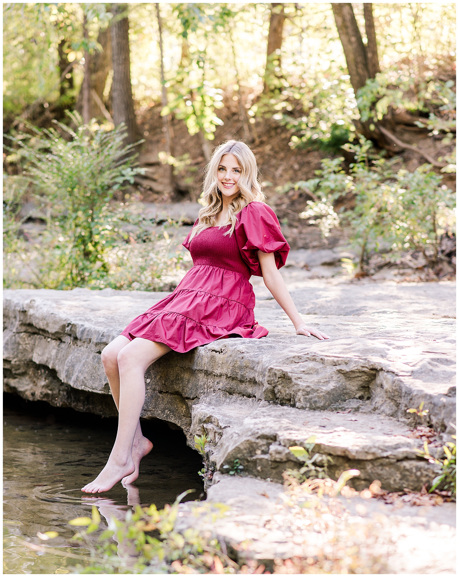 Nashville senior in cranberry dress, sitting on creek rocks.