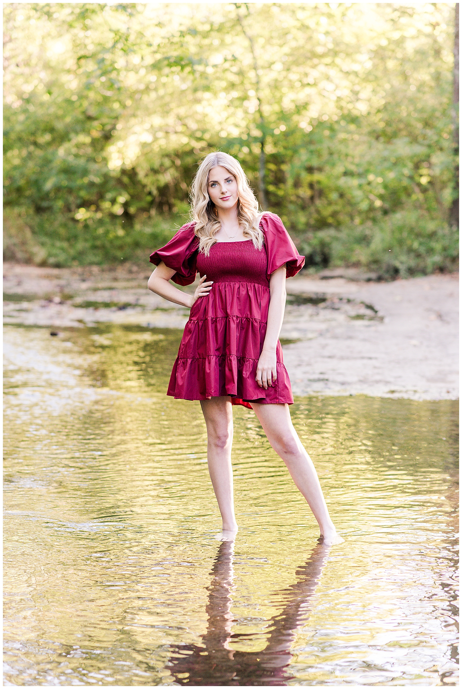 High school senior girl wearing a cranberry-colored dress, standing in the creek, at Ellington Agricultural Center.