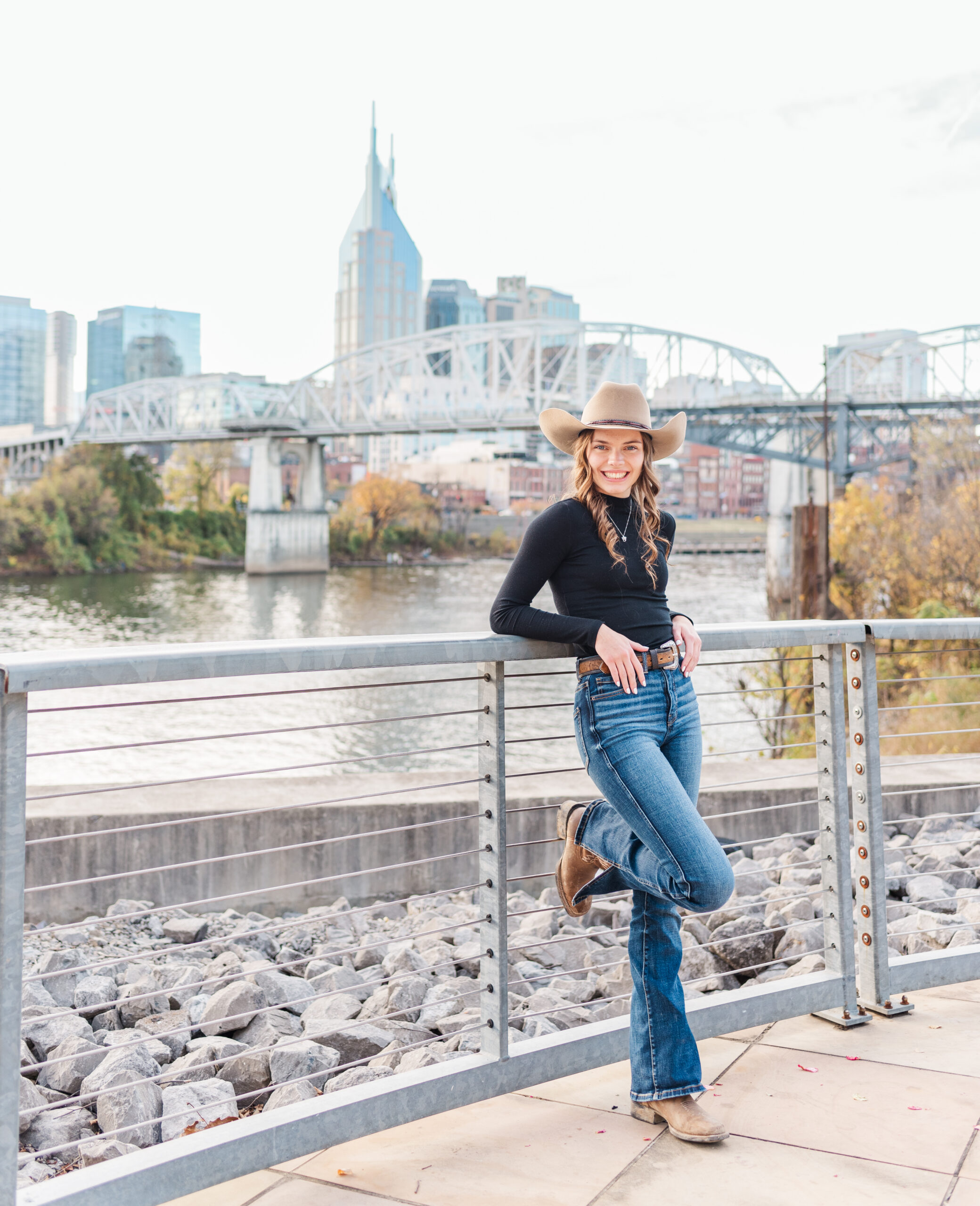 High school senior wearing jeans and a cowboy hat in standing in front of the Nashville skyline in Nashville, TN