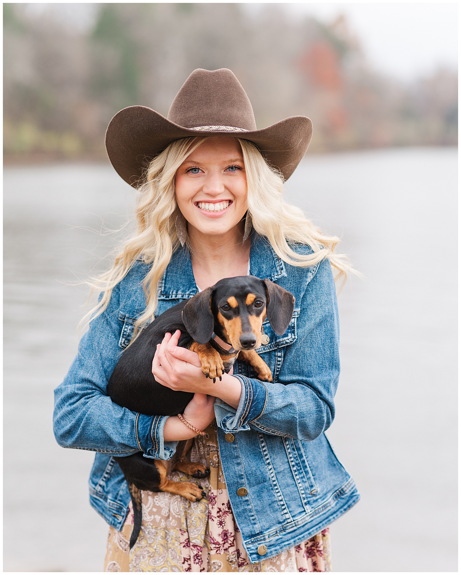 High school senior girl wearing a cowboy hat, holding her dachshund at Old Hickory Lake.