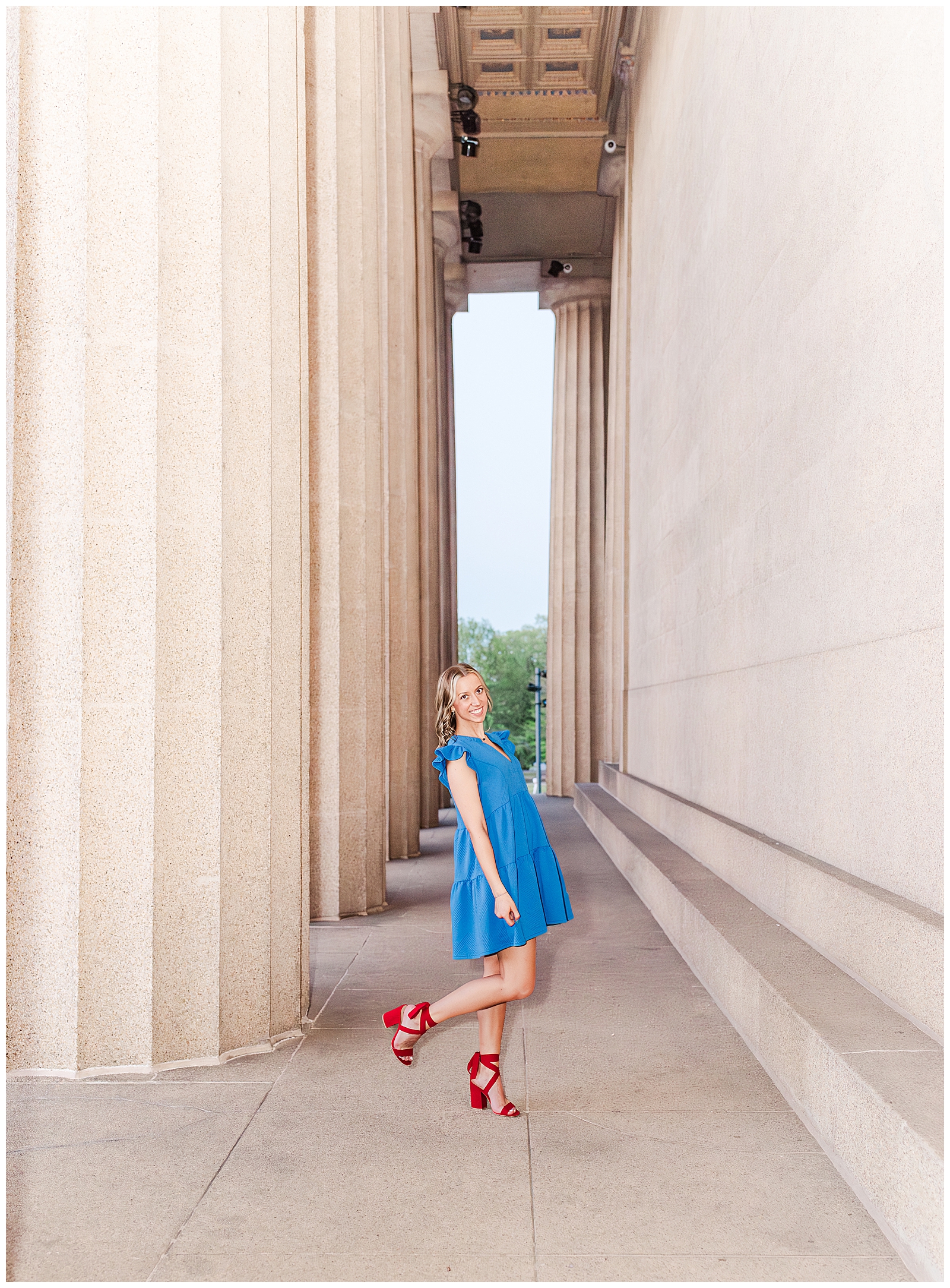 Senior girl in a blue dress and red heels, in front of columns at Centennial Park, Nashville, TN