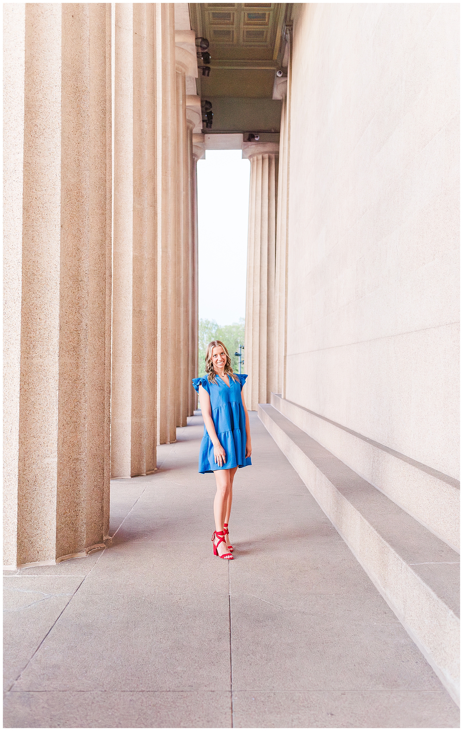 Senior girl in a blue dress and red heels, in front of columns at Centennial Park, Nashville, TN