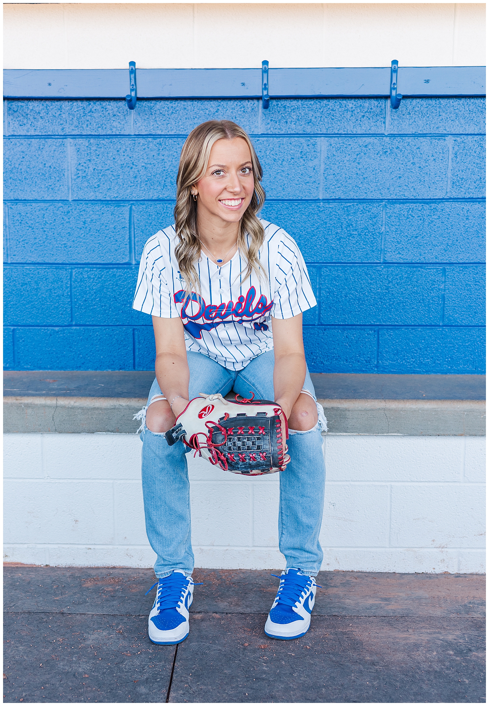 Senior girl holding her glove, sitting in the dugout of her high school softball team. 